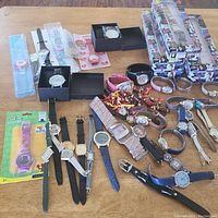 Photo showing a collection of vintage watches of various styles, some in packaging, some loose, placed on wooden table.