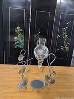 Front view of vintage glass wine decanter with etched floral design and metal holder with vine and leaf motifs on a wooden table.