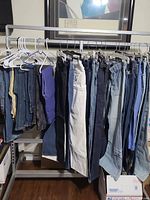 Photo showing multiple pairs of women's jeans hung on a rack in various colors including dark blue, light blue, black, and white.