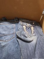 Photo of back pockets of blue denim jeans showing embroidery and metal studs typical of Miss Me brand