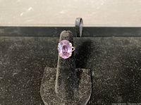 Front view of ring on black velvet stand showing oval purple stone and six prong setting