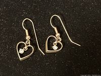 Two earrings displayed on black background showing open heart design and white stones
