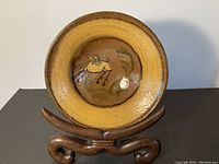 Front view of pottery bowl on wooden stand showing yellow glazed rim and central decorative design.