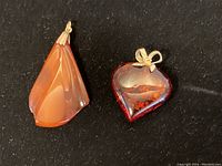 Two amber pendants on black background showing heart-shaped and elongated designs.