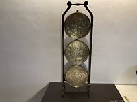 Full view of antique plant stand showing three vertically mounted round embossed metal plates in a wooden frame.