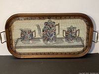 Full view of wooden framed rectangular tea tray with needlepoint embroidery of tea set design under glass