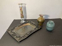 Four art glass pieces displayed against black background: three vases and one metal tray.