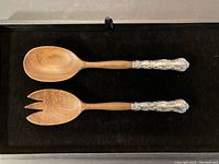 Top view of wooden spoon and fork salad servers with silver handles on black background.
