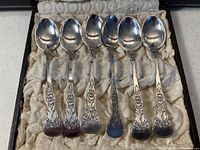 Front view of six polished silver spoons with decorative floral handles, neatly arranged in the box.