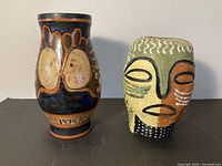 Front view of both pottery pieces on black surface against gray wall