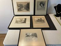Overview photo of all 5 framed etchings on table, showing varying subjects including buildings, portrait, and a docks scene
