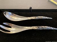Pair of Haida salad servers, metal spoon and fork with detailed tribal carvings on handles.