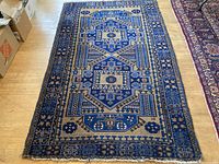 Full view of the Persian wool rug laid out on a wood floor showing the entire length and main geometric pattern.