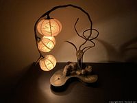 Korean paper flower lamp illuminated showing three rice paper spherical shades attached to a metal branch on wood-like base.