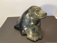 Front view of dark green-black stone seal sculpture on black mat against white wall