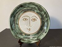 Full front view of pottery plate with stylized face design and green swirled glaze.
