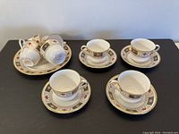 Thirteen pieces of Royal Crown Derby tea set, with cups, saucers, and plates arranged on black table.