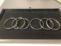 Six slender silver bangles arranged on a black velvet surface inside a display tray.