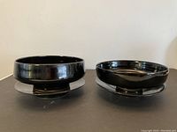 Two black glaze studio pottery bowls on matching plates shown from side angle.