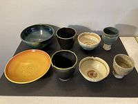 Overview of all 8 pottery bowls and cups showing different sizes, colors, and shapes on a black surface.
