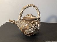 Side angle view of studio pottery tea pot showing textured surface, curved spout and handle.
