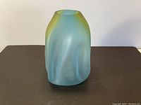 Front view of a matte frosted art glass vase with blue and yellow hues on a black surface