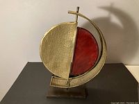 Front view of vintage lamp showing brass semi-circle with textured finish and red leather panel, mounted on brass base.