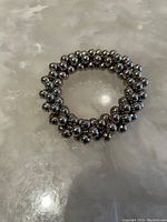 Metallic beaded bracelet shown on a reflective marble surface, front view.