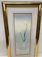 Front view of vertical art print showing two white tulips in white glass vase with brass frame, against white background.