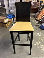 Full view of the bar stool showing the black wooden frame and beige leather seat.