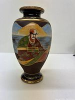 Front view showing a painted figure of a man in traditional clothing, seated, with a mountainous landscape in the background.