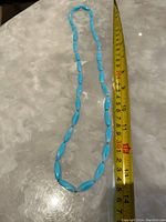 Photo showing turquoise stone necklace next to tape measure for sizing, confirming length around 14 inches.
