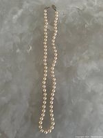 Pearl necklace laid out on a textured surface, showing length and overall design