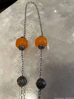 Shows entire necklace chain with two large orange beads and silver ornate bead caps, plus smaller silver filigree beads.