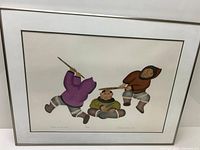 Framed Inuit stencil art showing three figures in traditional clothing with spears, signed and numbered.