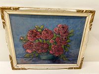 Full view of signed floral oil painting on board, showing bunch of pink/red roses in a teal vase, framed in distressed white/gold frame.