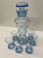 Blue glass decanter with stopper surrounded by six glasses, showing the polka dot design clearly and the lot contents.