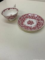 Side angle view of a red and white decorative Coalport teacup and saucer with gold trim