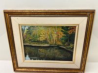 Framed oil painting showing whole artwork with autumn forest and river scene in gold and cream frame.