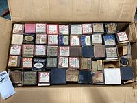 Top-down view of many antique player piano rolls arranged neatly in a cardboard box, showcasing various brand labels including QRS, Aeolian, and others.