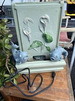 Full view of the concrete koi fish fountain showing two blue-gray koi fish and the floral relief design on the back panel, also displaying the attached electric cord.