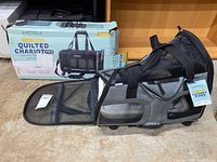 Photo of the open box showing the black quilted pet carrier with the front mesh panel opened out flat and the original box in the background.