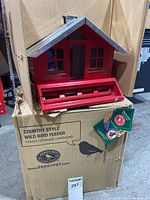 Photo of the red Country Style wild bird feeder on top of its original Perky-Pet branded box with packaging tags attached.