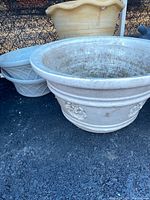 Large beige scalloped rim pot and two off-white pots with floral medallions at front with other pots partially visible