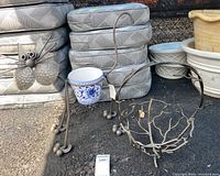 Outdoor metal cat-shaped planter holding a blue and white ceramic flower pot next to a metal vine open basket.