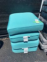 Stack of four teal outdoor seat cushions, showing their size and color.