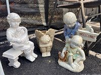 Ceramic statues and angel planter together in outdoor setting