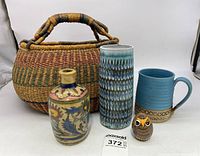 Front view of the five-item grouping: ceramic pottery in various shapes and designs, owl figurine, and woven basket behind