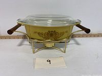 Front view showing the Pyrex casserole bowl with lid on gold-tone candle caddy, wooden handles visible.