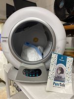 Front view of the spherical litter box showing interior, control panel buttons, and instruction manual propped at front